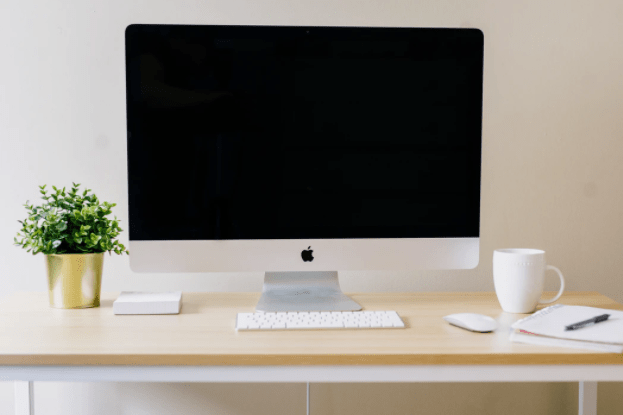 A clean desk with a computer monitor, a notebook, and a cup