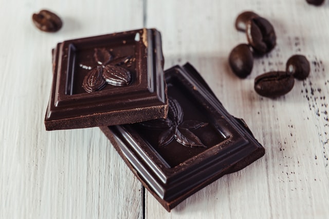 Pieces of dark chocolate on a white table with Coco Nibs