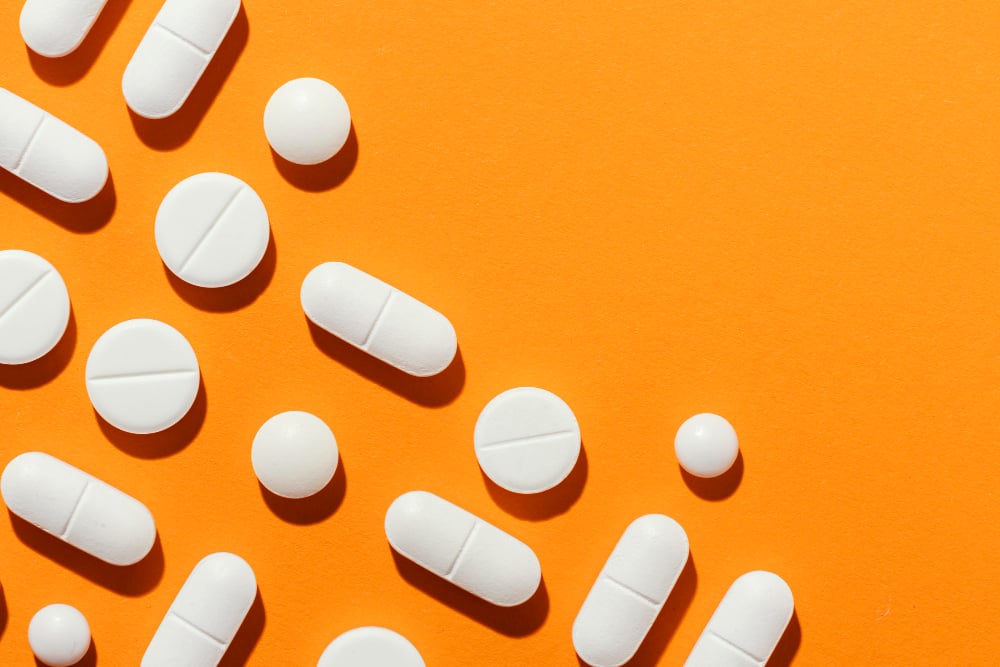 Pills in tablet form laid out on an orange background. 