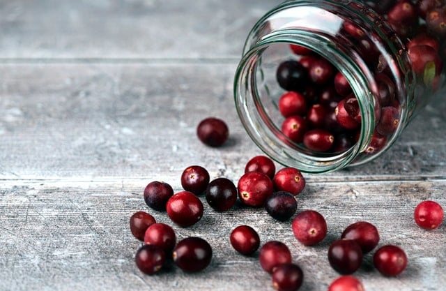 A jar of antioxidant rich cranberries spilling out onto a table.