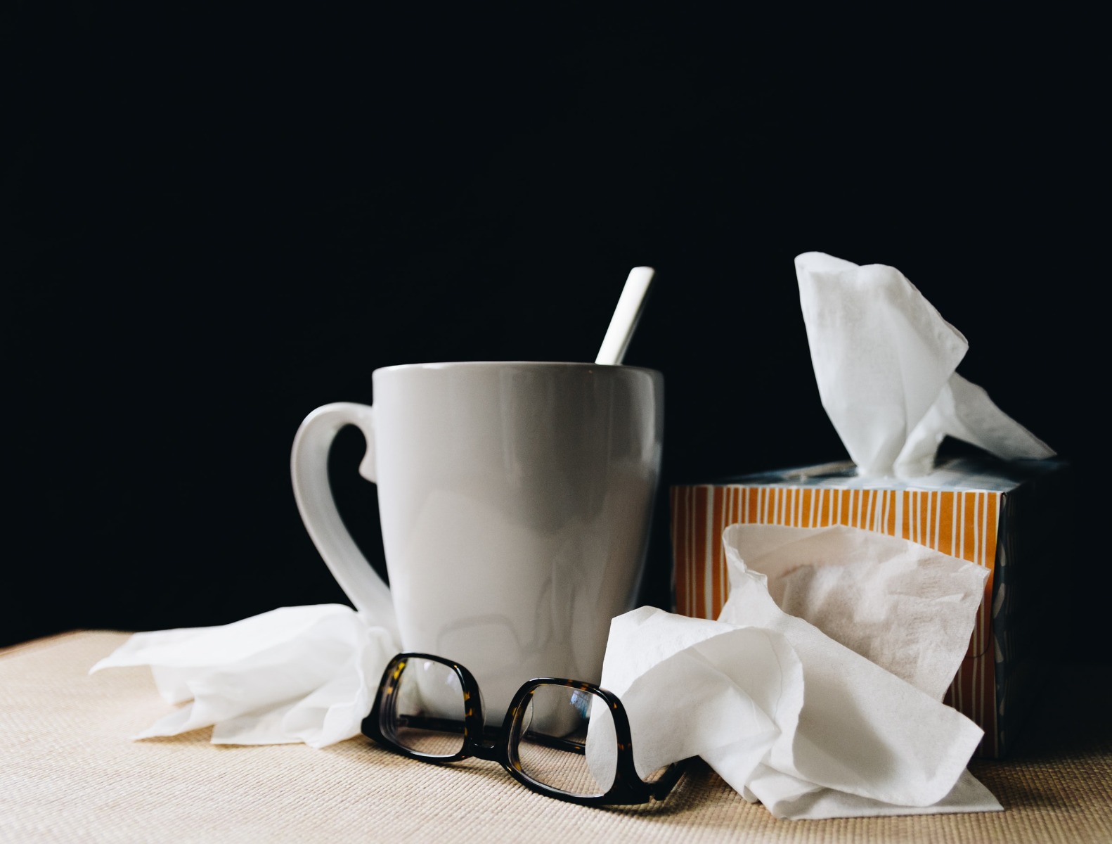 Kleenex, cup of tea and glass beside the bed of a sick person